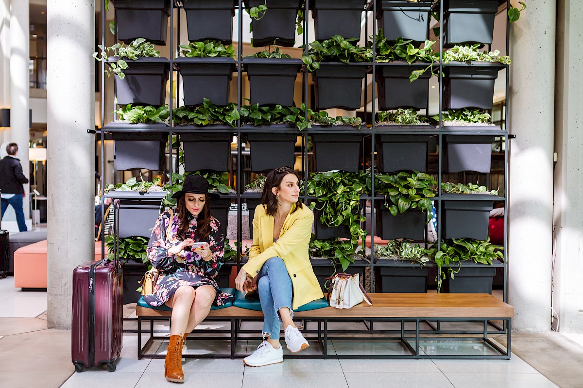 Two people sit on a bench with luggage, surrounded by a vertical garden.