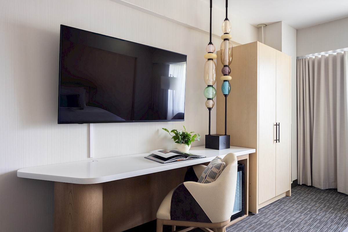 A modern room with a wall-mounted TV, a desk with an open book, a potted plant, and decorative hanging lights.