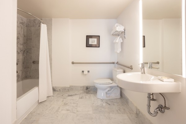 A clean, accessible bathroom with a bathtub, toilet, sink, and towel racks.