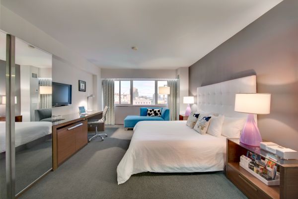 A modern hotel room with a large bed, lamps, desk, TV, and a window with city views. A blue couch sits near the window, ending the sentence.