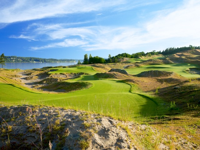 A scenic golf course with lush green fairways and rolling hills under a blue sky with scattered clouds.