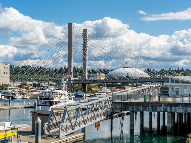 The image shows a marina with boats, a bridge, and a domed building in the background under a partly cloudy sky.