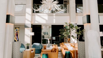 A spacious hotel lobby features modern furniture, a large chandelier, and natural light streaming through windows.