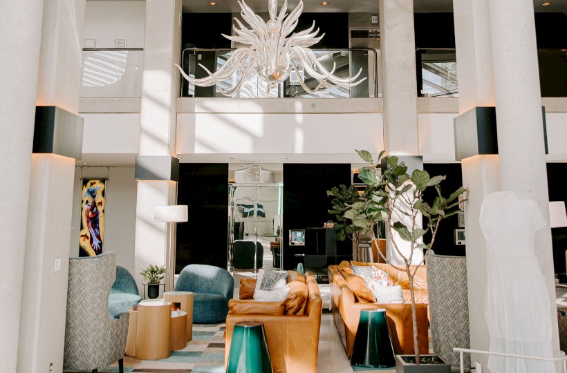 A spacious hotel lobby features modern furniture, a large chandelier, and natural light streaming through windows.