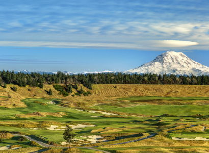 The image shows a scenic golf course with a mountain in the background under a partly cloudy sky, surrounded by lush greenery and some trees.