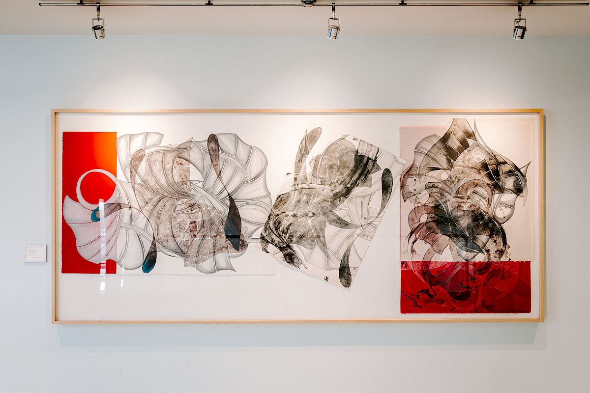 A framed abstract artwork featuring a mix of organic shapes, black and white details, and bold red sections, displayed under gallery lights.