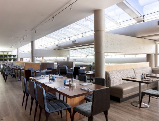 A spacious, modern restaurant interior with large windows, wooden tables, and stylish chairs, ready for diners to enjoy a meal.
