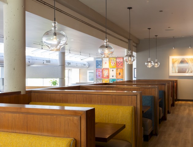 This image shows a cozy dining area with wooden booths, hanging glass lights, and colorful artwork on the walls in a modern restaurant.