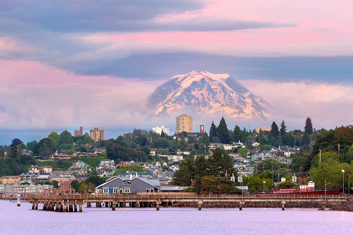 A scenic seaside town with shoreline houses, calm waterfront views, and a snow-capped mountain under a pink sky, featured in Hotel Murano’s Black Friday 2025 and Cyber Monday Cyber Sale promotions.