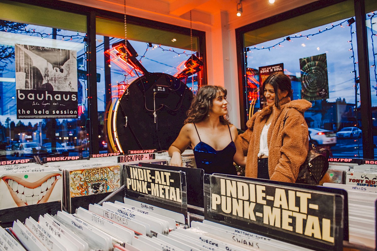 Two women in a record store talking, surrounded by vinyls labeled 