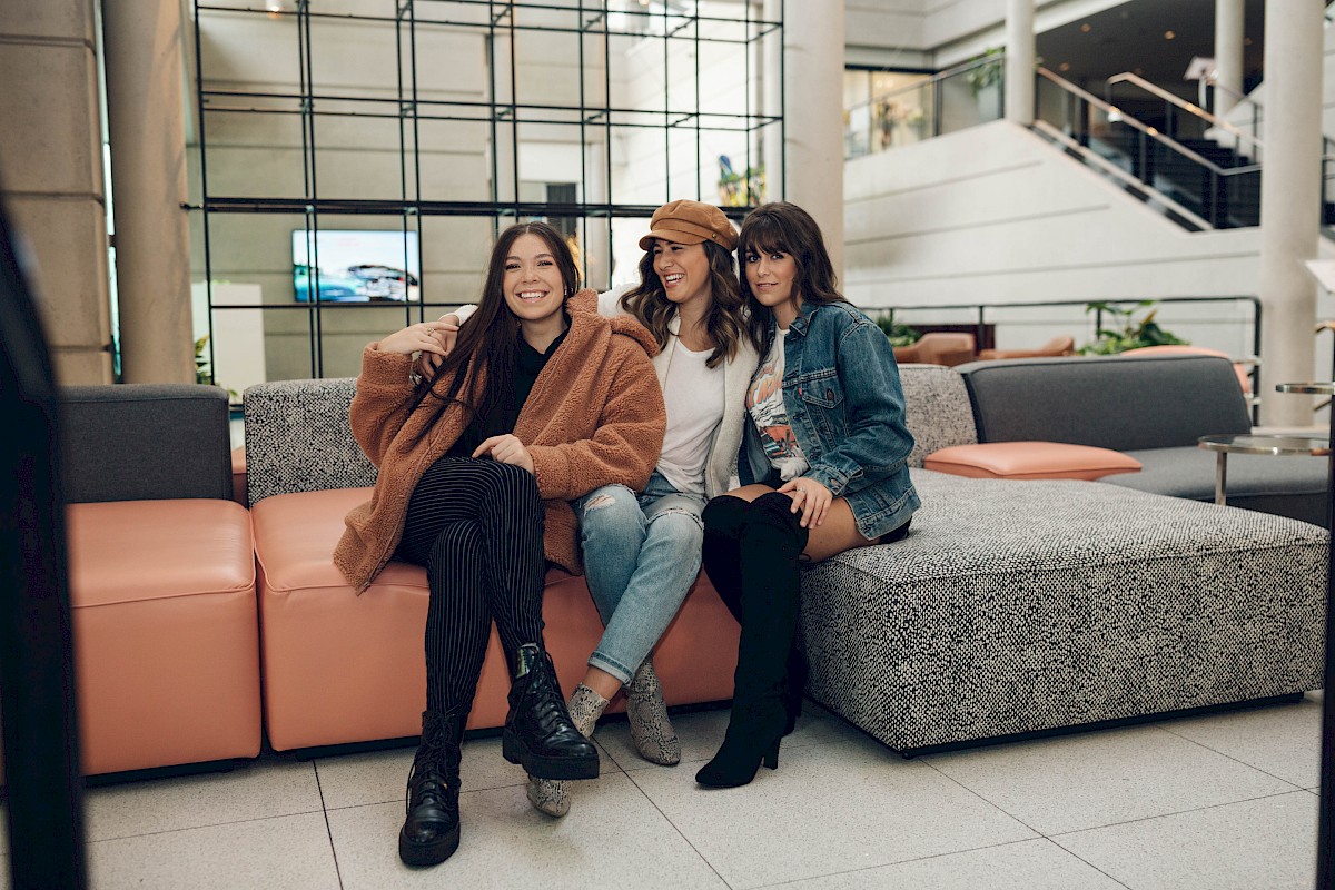 Three people are sitting on a modern couch in a stylish indoor setting, smiling and posing for a photo.