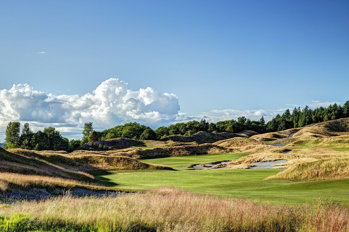A scenic landscape of a golf course with rolling hills, lush greenery, and a partly cloudy sky under a clear blue expanse ends the sentence.