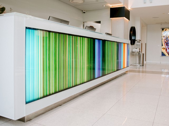 A modern reception desk with colorful, vertical light strips and a white and minimalist design in a clean, bright lobby.