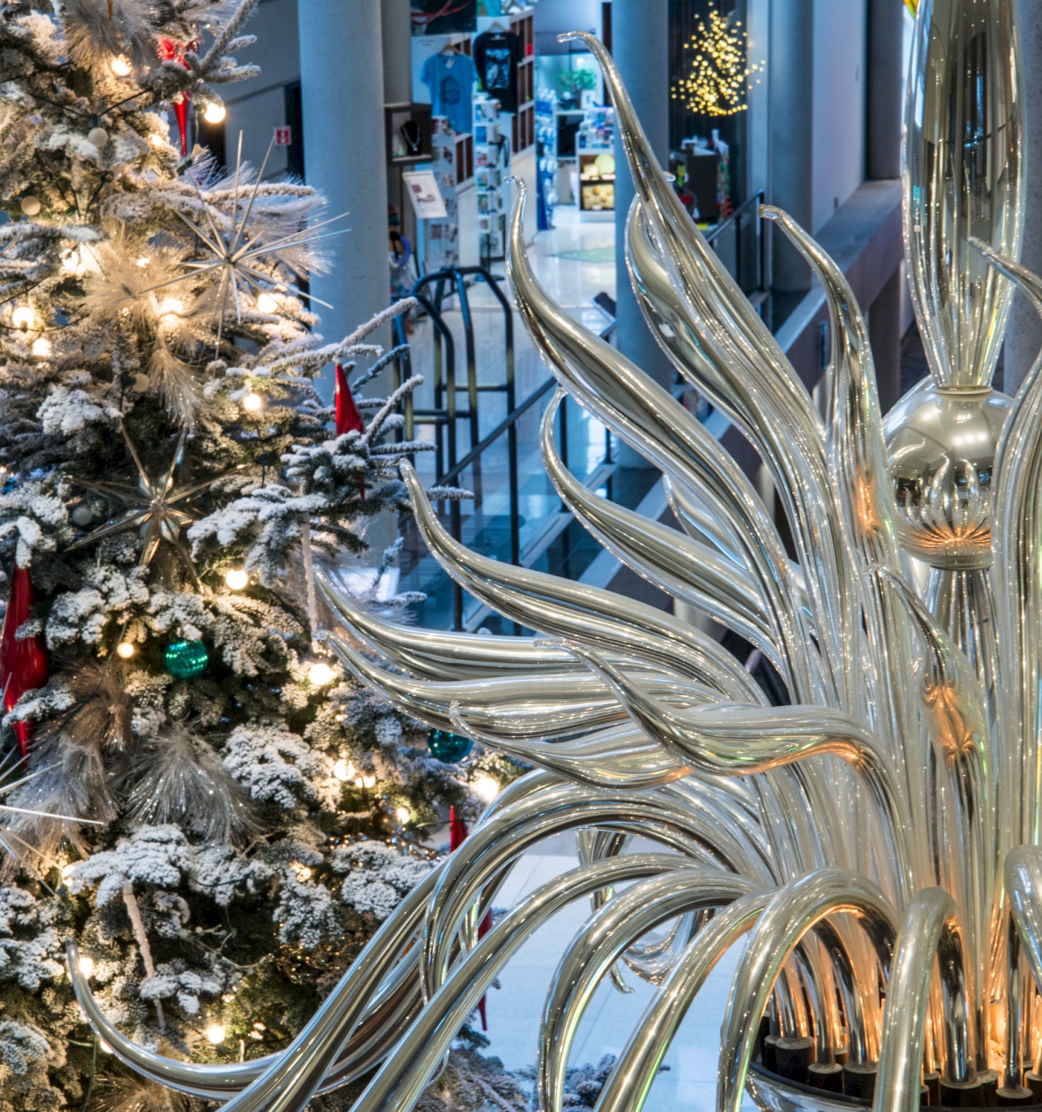 A festive indoor scene with a snow-dusted Christmas tree and a striking metallic palm sculpture, holiday decor sparkling softly.
