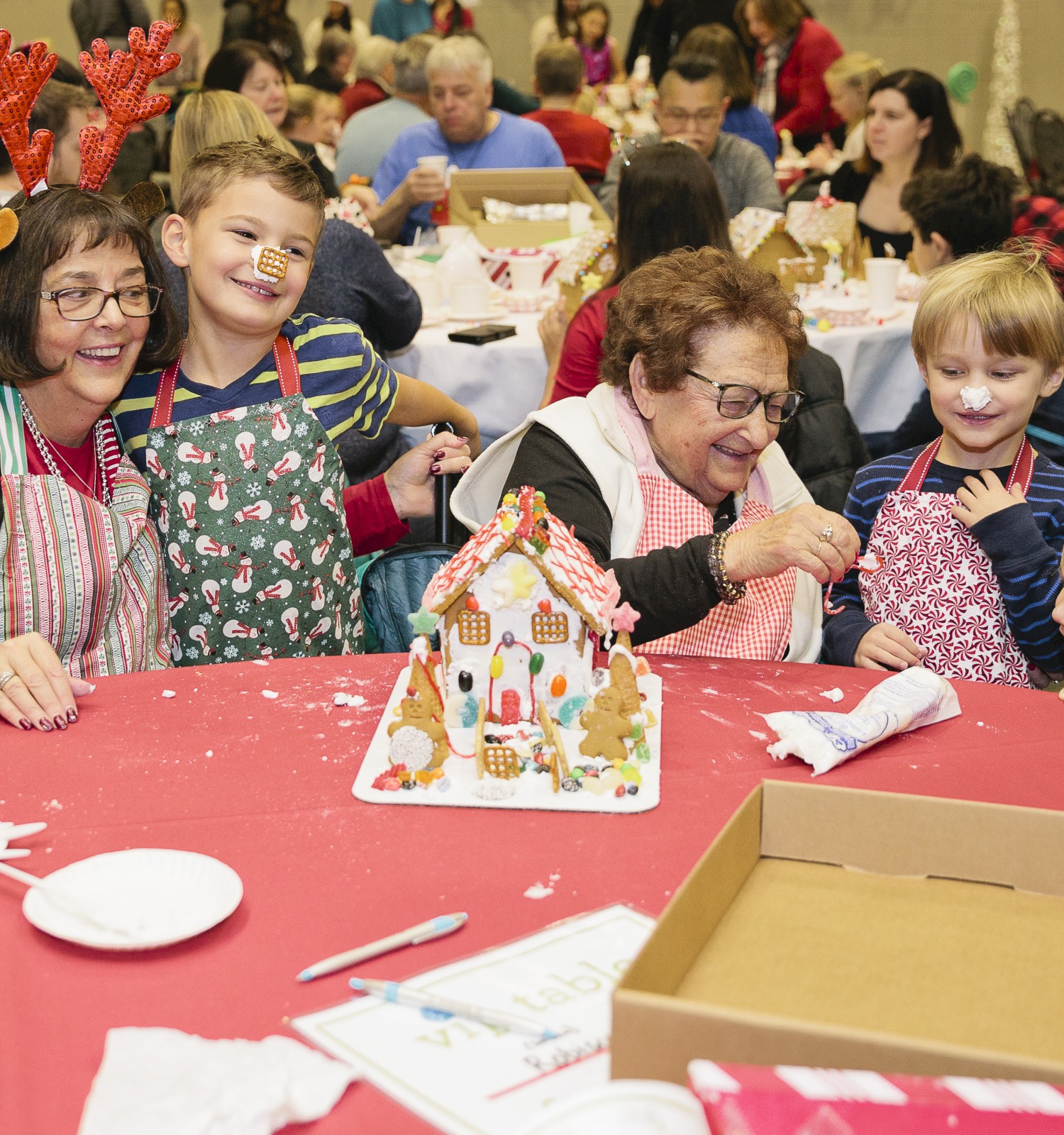 A festive crafting scene with kids at a table making gingerbread house decorations, smiling and sharing a joyful holiday moment. Top it at 140 characters, always ending the sentence.