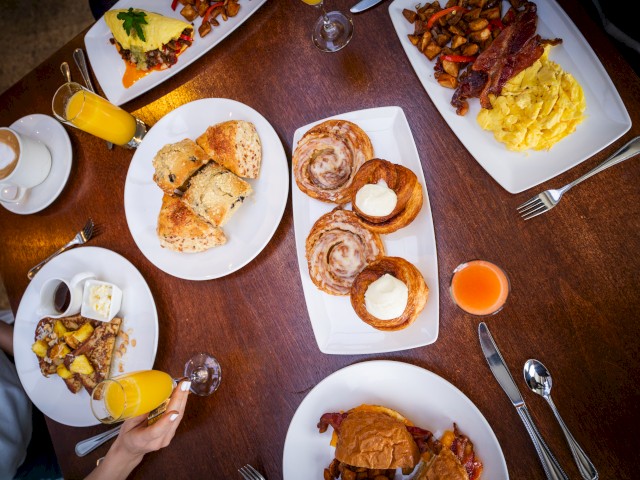 The image shows a breakfast spread including orange juice, pastries, scrambled eggs, roasted potatoes, coffee, and a variety of breakfast dishes.
