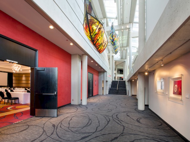 A modern hallway with red accent walls, abstract paintings, and a connected conference room on the left, leading to a staircase.
