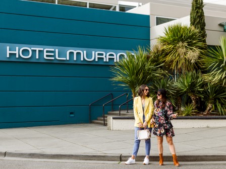 Two people stand in front of the Hotel Murano, next to plants on a sidewalk.