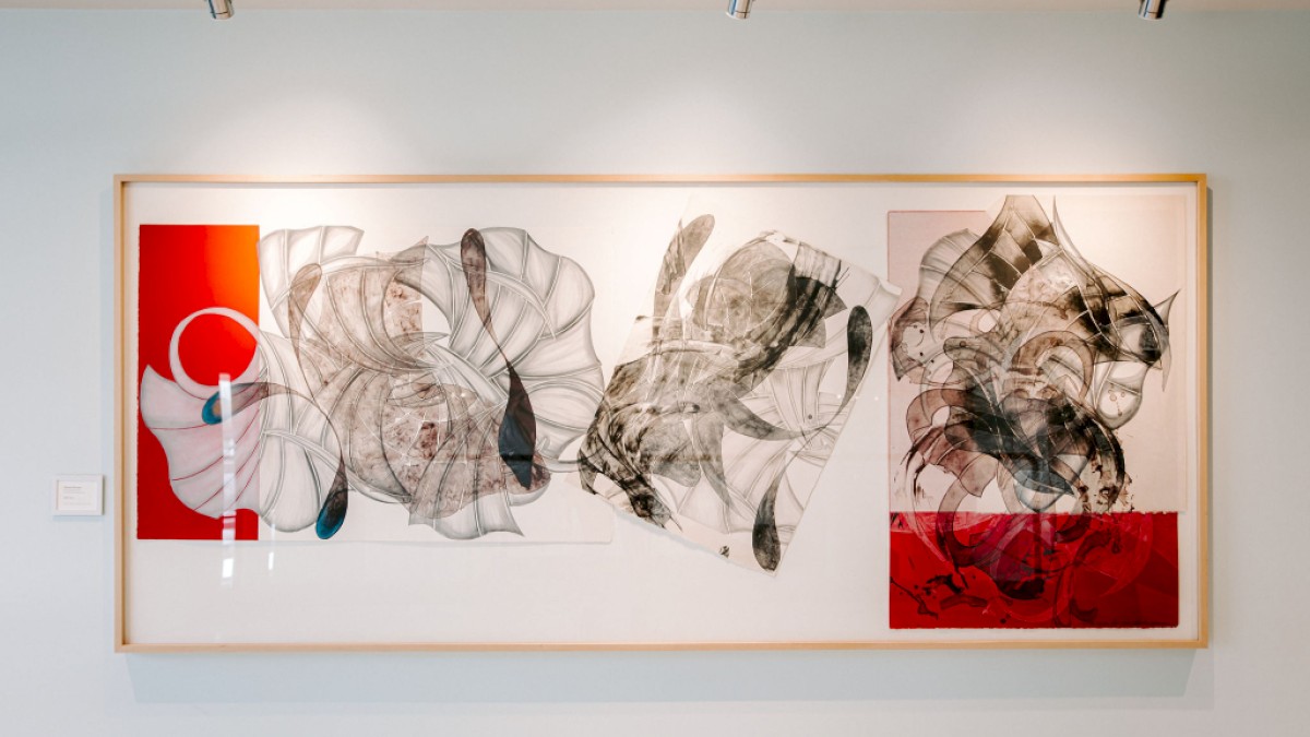 The image shows an abstract artwork with swirling lines and shapes, layered over red and white backgrounds, framed and hung on a wall.