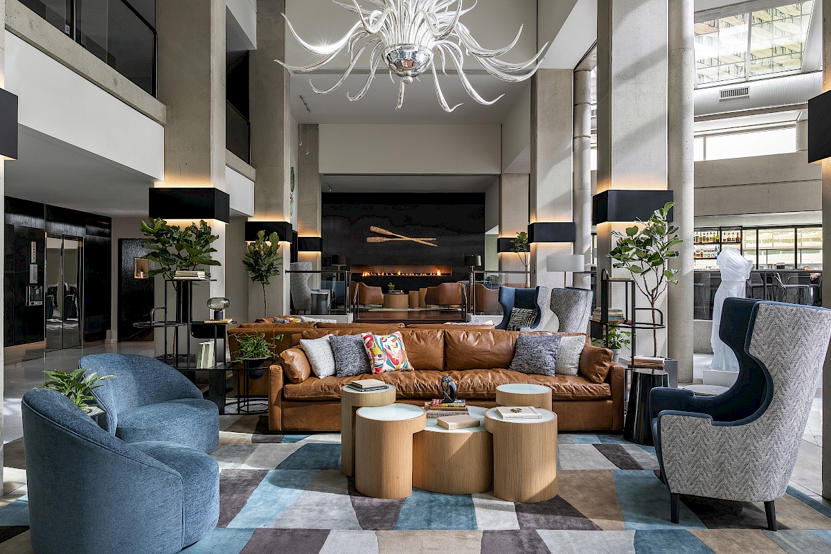 A modern lobby with stylish furniture, blue and brown tones, a chandelier, and a colorful rug, creating an inviting atmosphere.