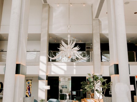 Modern hotel lobby with a chandelier, seating area, and large floor-to-ceiling windows that let in natural light.
