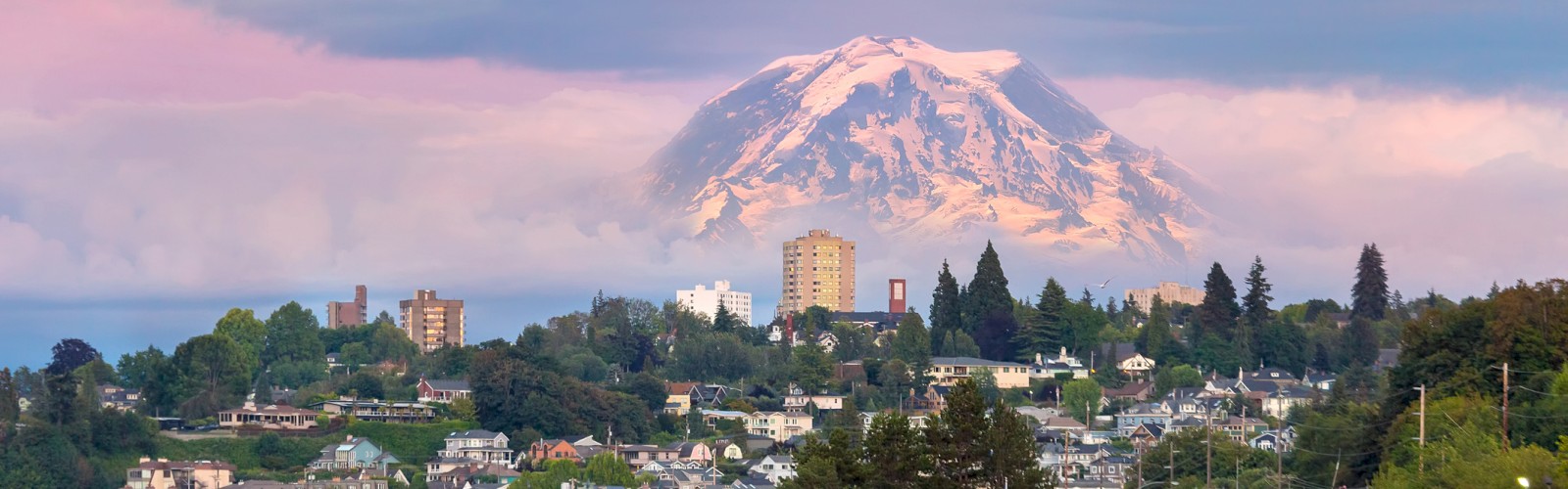 A scenic view of a city with a snow-capped mountain in the background during sunset or sunrise.