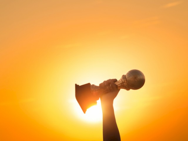 A hand holding a trophy against a sunset sky, symbolizing victory or achievement.