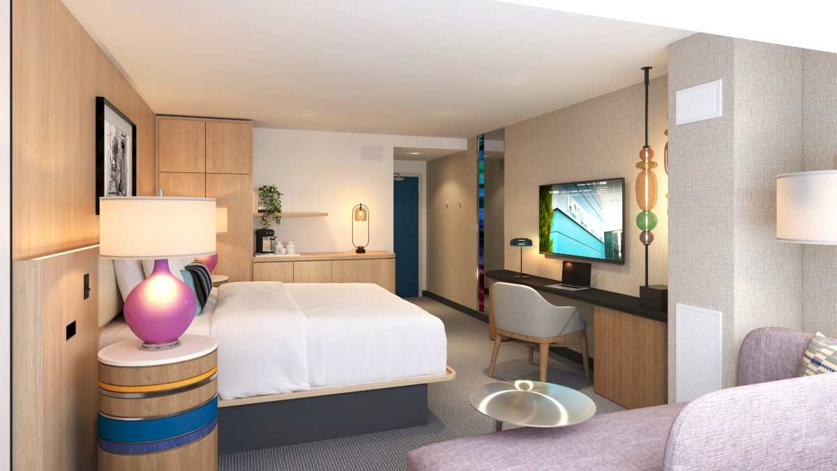 A modern hotel room features a cozy bed, colorful decor, a TV, and a workspace with a desk and chair in a stylish, well-lit setting.