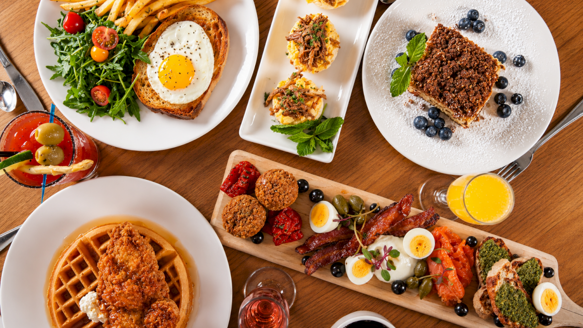 A variety of dishes including pasta, salad, desserts, appetizers, and drinks spread on a wooden table.