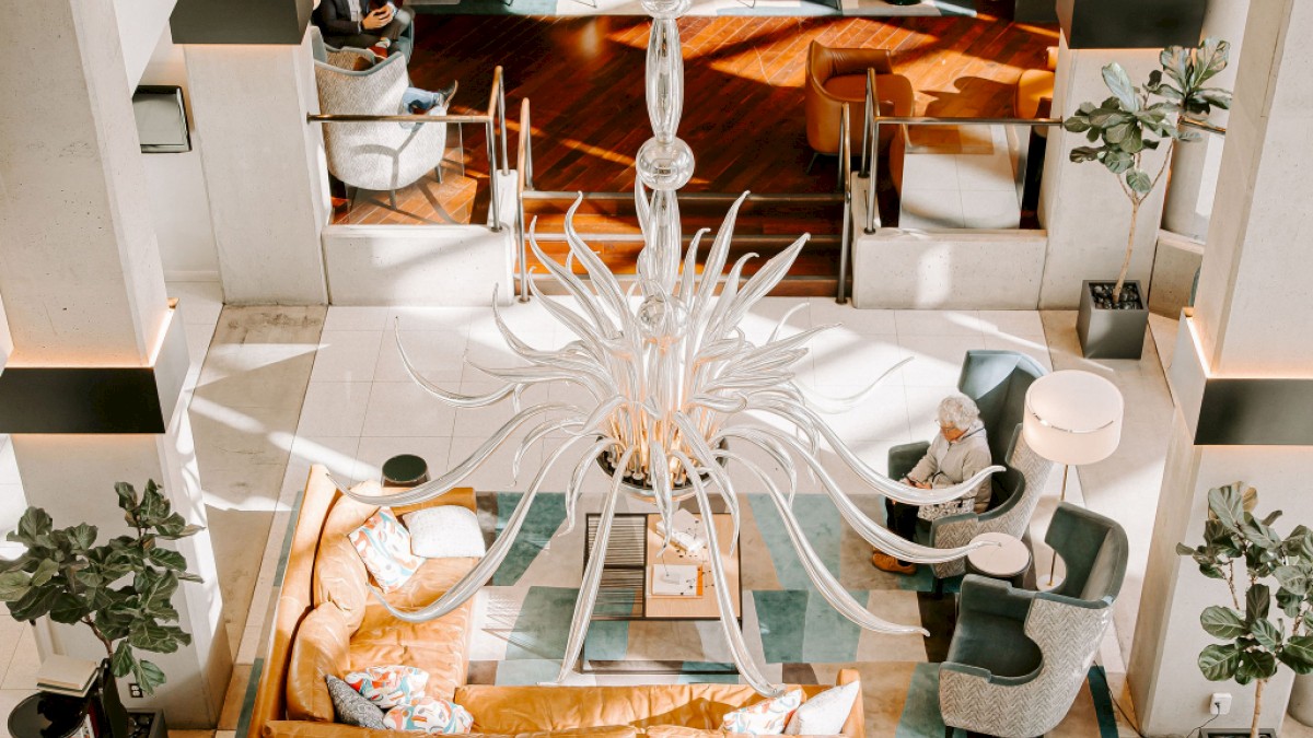 A luxurious hotel lobby with stylish seating, a chandelier, and two people relaxing in a modern, well-lit space.