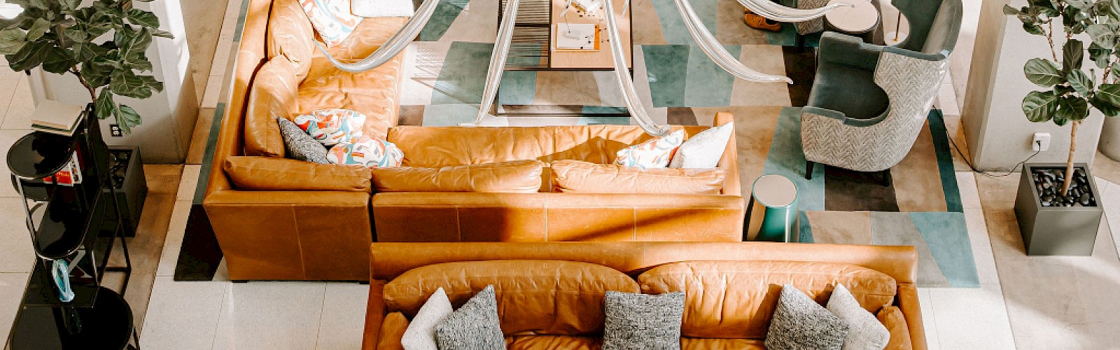 The image shows a stylish lobby with modern furniture, a large chandelier, and two people seated and reading.