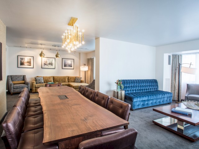 A stylish living and dining area with modern furniture, including a large wooden table, velvet sofa, armchairs, and decorative lighting.