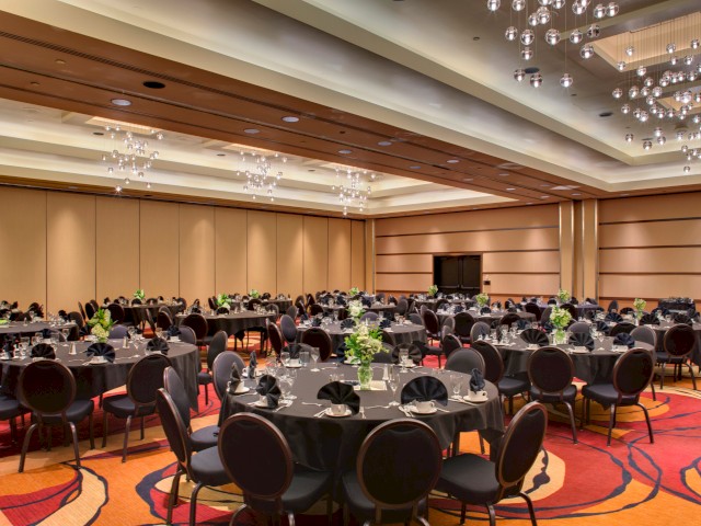 This is a banquet hall set for a formal event with round tables, black tablecloths, and floral centerpieces.