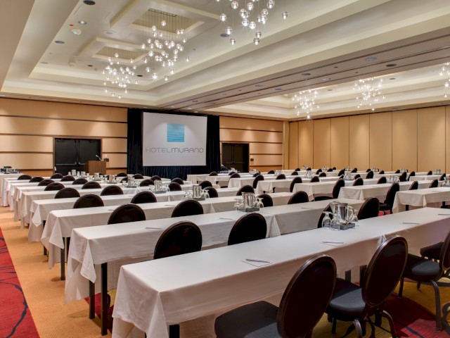 A conference room set up with long tables, chairs, water pitchers, glasses, and a projector screen displaying 